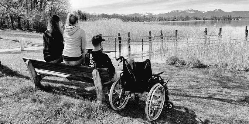 Menschen auf einer Bank am See mit Rollstuhl